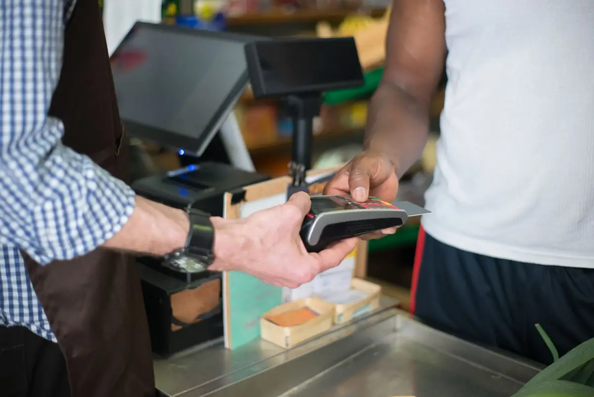 A shopkeeper holding a card terminal while a customer pays with a bank card.